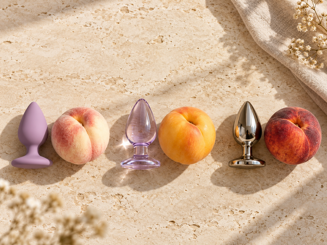 Silicone, glass, and stainless-steel butt plugs arranged with three different peaches to illustrate soft, smooth, and firm material differences.