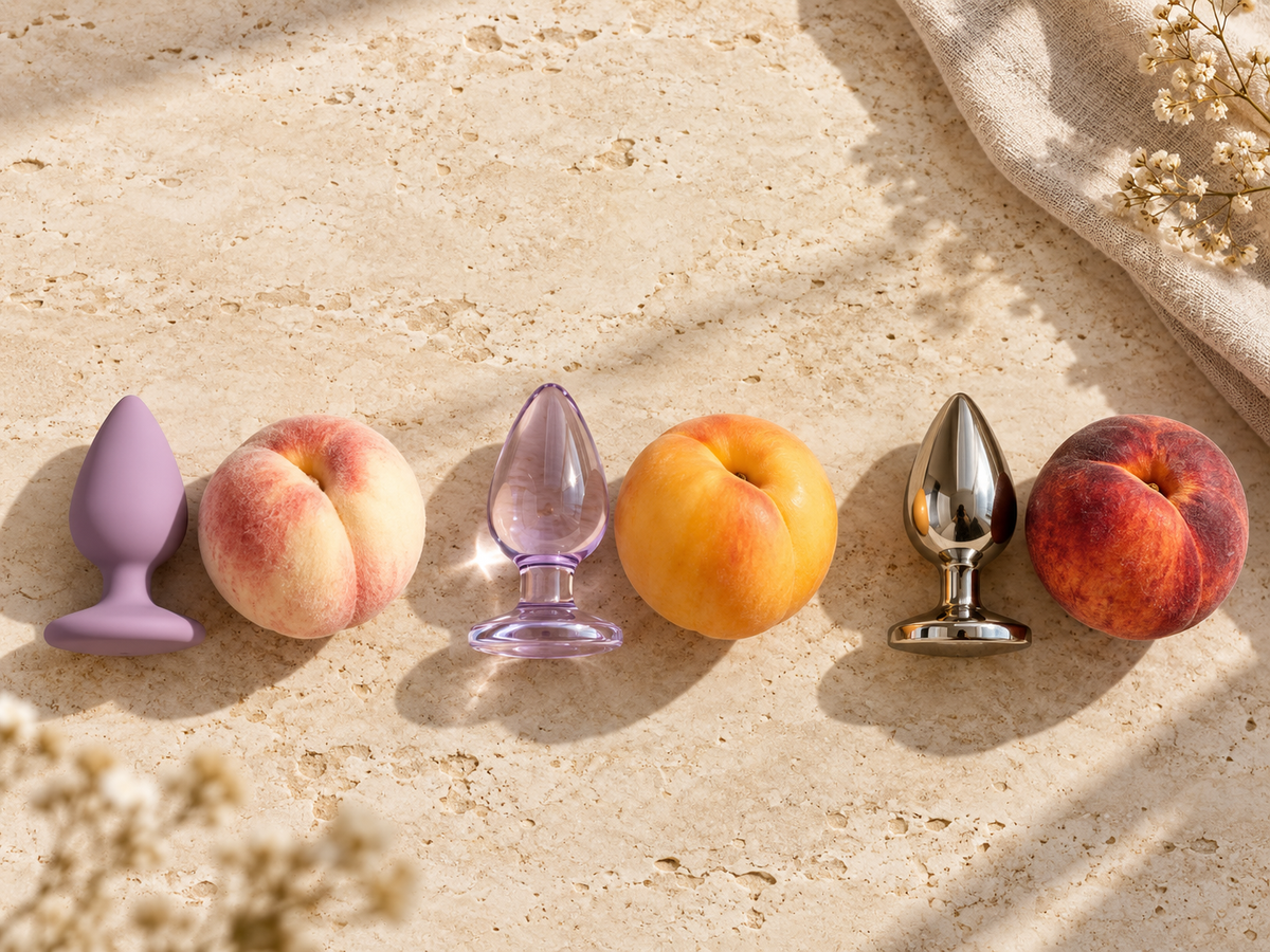 Silicone, glass, and stainless-steel butt plugs arranged with three different peaches to illustrate soft, smooth, and firm material differences.