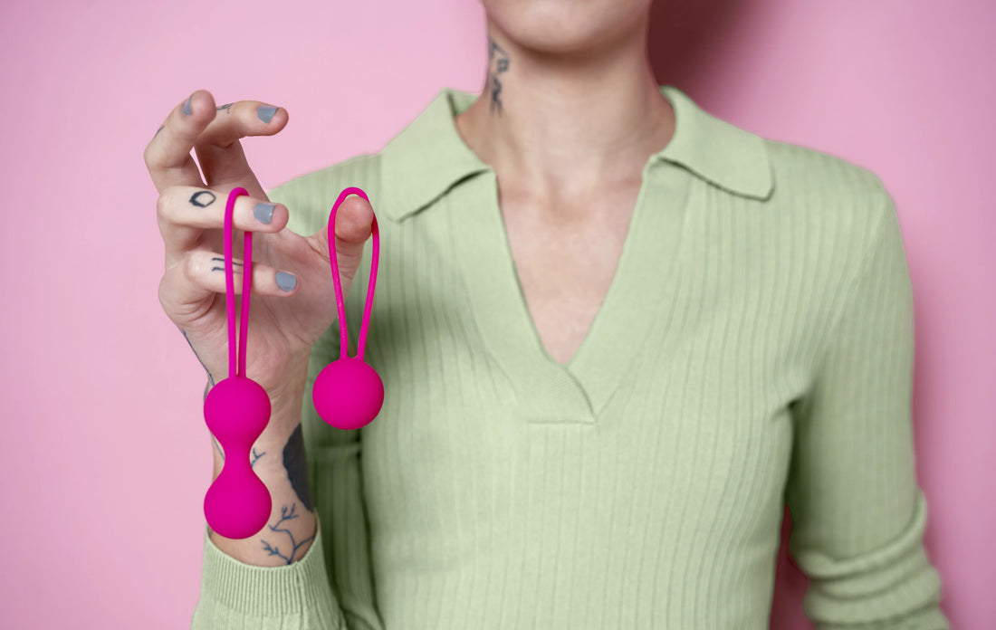 Person holding bright pink dual pleasure balls against a pink background.