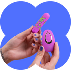 A person's hands holding a pink personal massager and its matching remote control against a blue graphic background. The massager has green leaf patterns, and the remote is pink with a gold accent ring.