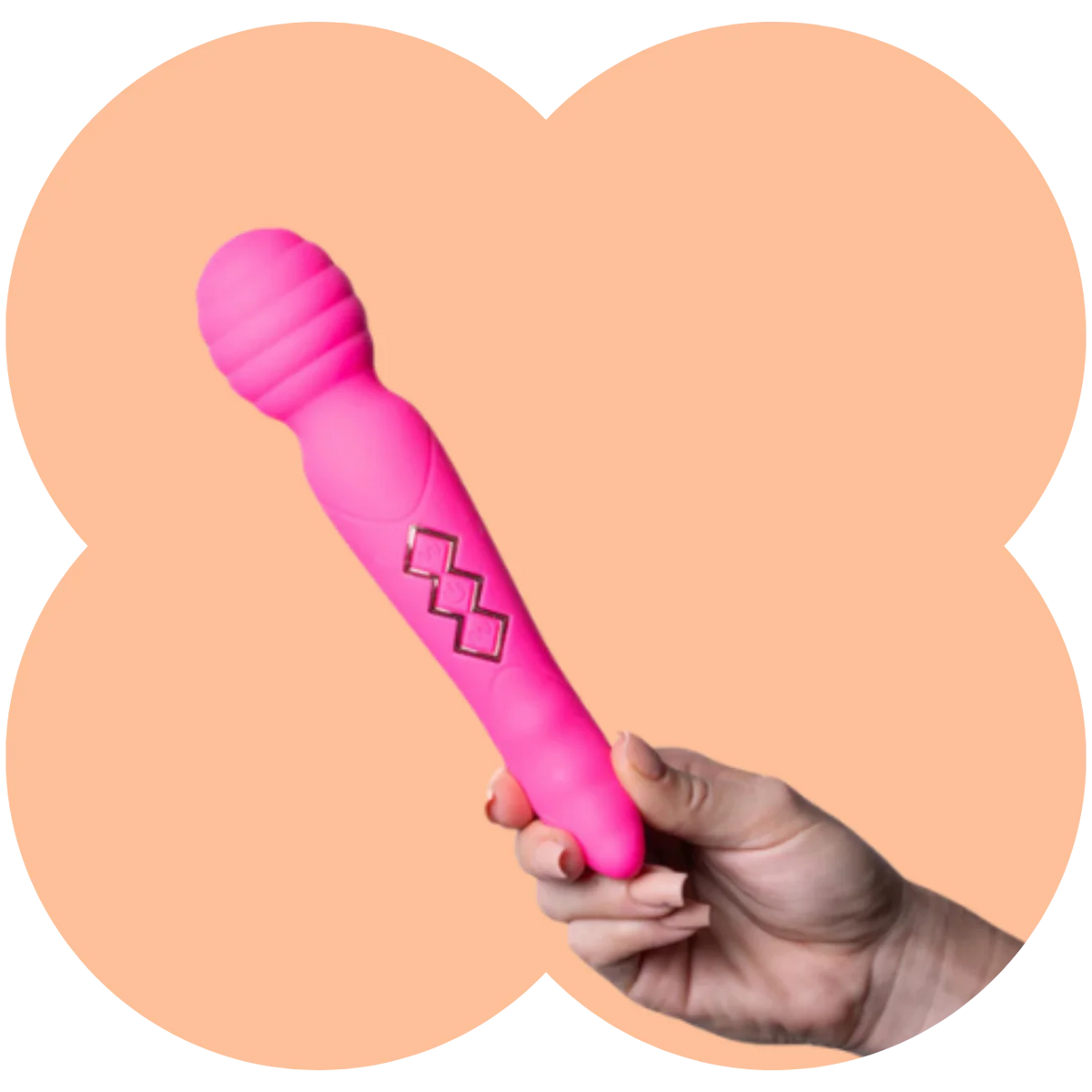 A hand holding a bright pink personal massager wand with a textured head and a geometric diamond design on the handle, set against a peach-colored four-petal background shape.